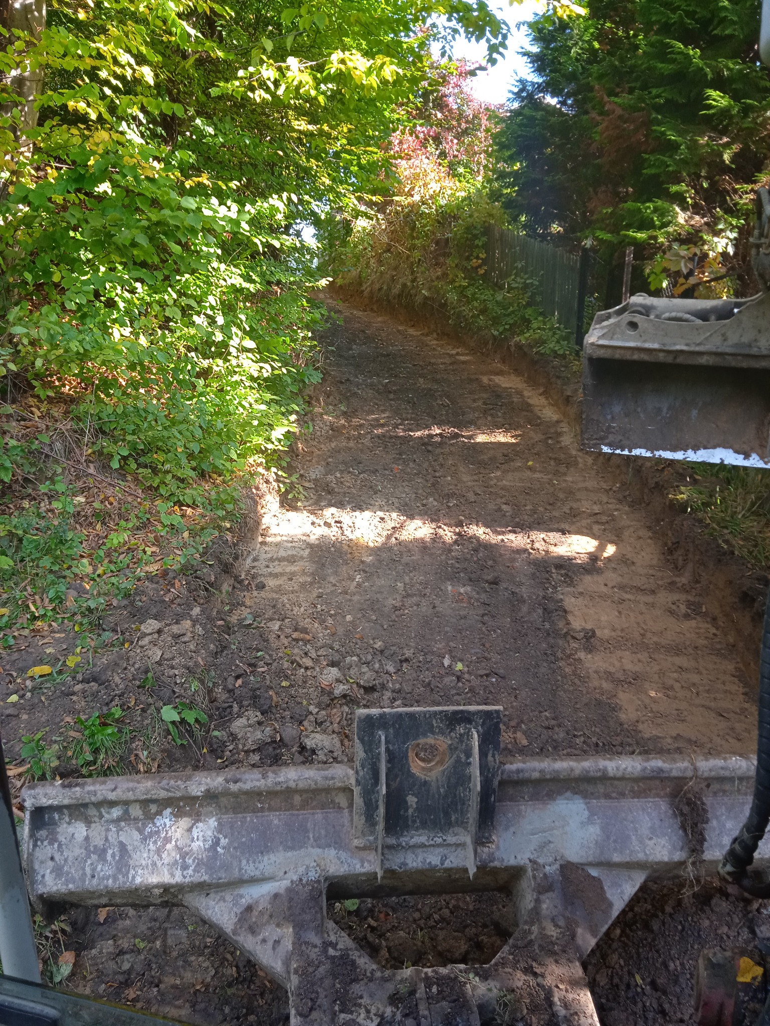 Wyrównany teren pod drogę leśną, widok z kabiny maszyny budowlanej, drzewa po bokach.