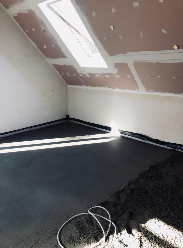 Wylewka betonowa w pokoju na poddaszu z oknem dachowym, widoczne przygotowane ściany i kabel na podłodze.
