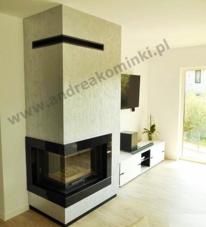 Nowoczesny kominek narożny z obudową w odcieniach szarości i czarnymi elementami wykończeniowymi, widoczny w jasnym salonie z telewizorem i białymi meblami.