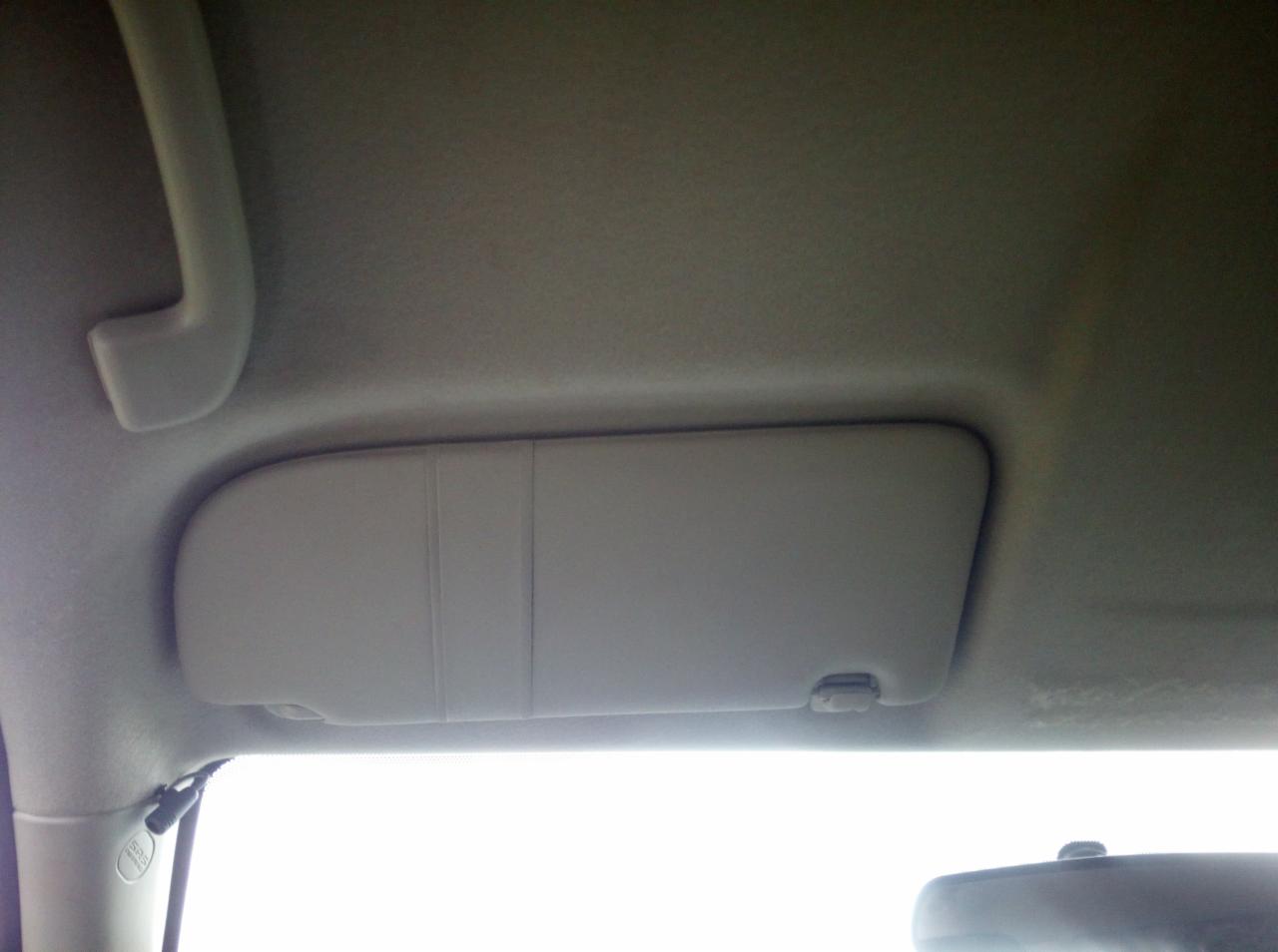Wnętrze samochodu z widoczną szarą osłoną przeciwsłoneczną przy suficie, uchwyt nad drzwiami i fragment lusterka wstecznego.