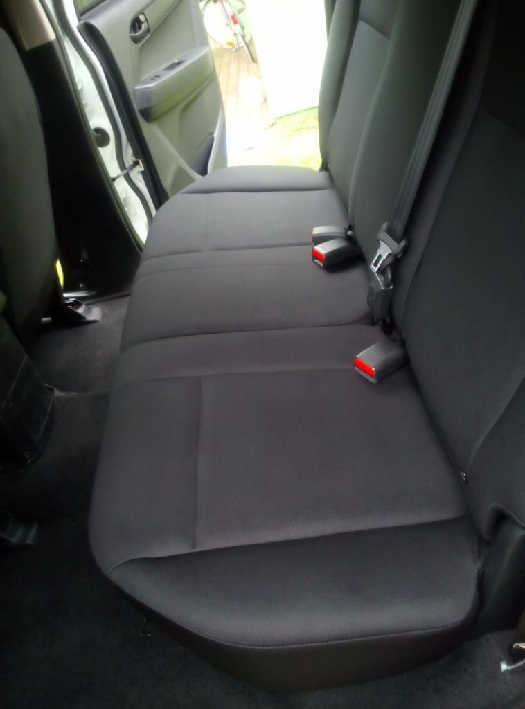 Wnętrze samochodu: tylna kanapa po wypraniu tapicerki, widoczne pasy bezpieczeństwa z czerwonymi elementami, czysta, ciemna tapicerka.