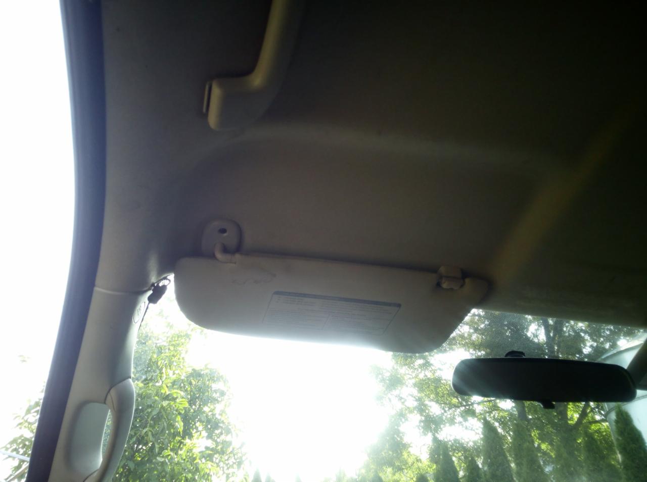 Wnętrze samochodu z opuszczonym daszkiem przeciwsłonecznym i widocznym lusterkiem wstecznym, z zewnątrz przebijające promienie słoneczne.