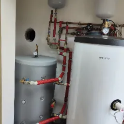 Dwa zbiorniki akumulacyjne ciepła, jeden marki Rotenso, połączone rurami z izolacją termiczną, widoczne elementy instalacji grzewczej w pomieszczeniu technicznym.