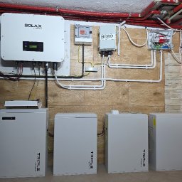 FotonSolar - Kompletna instalacja fotowoltaiczna w pomieszczeniu: falownik Solax Power, moduły Nord i cztery moduły Triple Power. Widoczne przewody i rury instalacyjne.