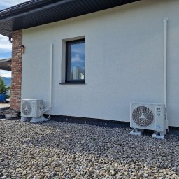 FotonSolar - Dwa klimatyzatory zewnętrzne zamontowane na elewacji domu, z widocznymi rurami odprowadzającymi. Tło stanowi elewacja i kamieniste podłoże.