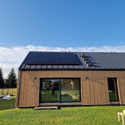 FotonSolar - Elegancki dom z panelami słonecznymi na szarym dachu, widok z trawnika z małym stolikiem i serwisem do herbaty. Błękitne niebo z chmurami w tle.