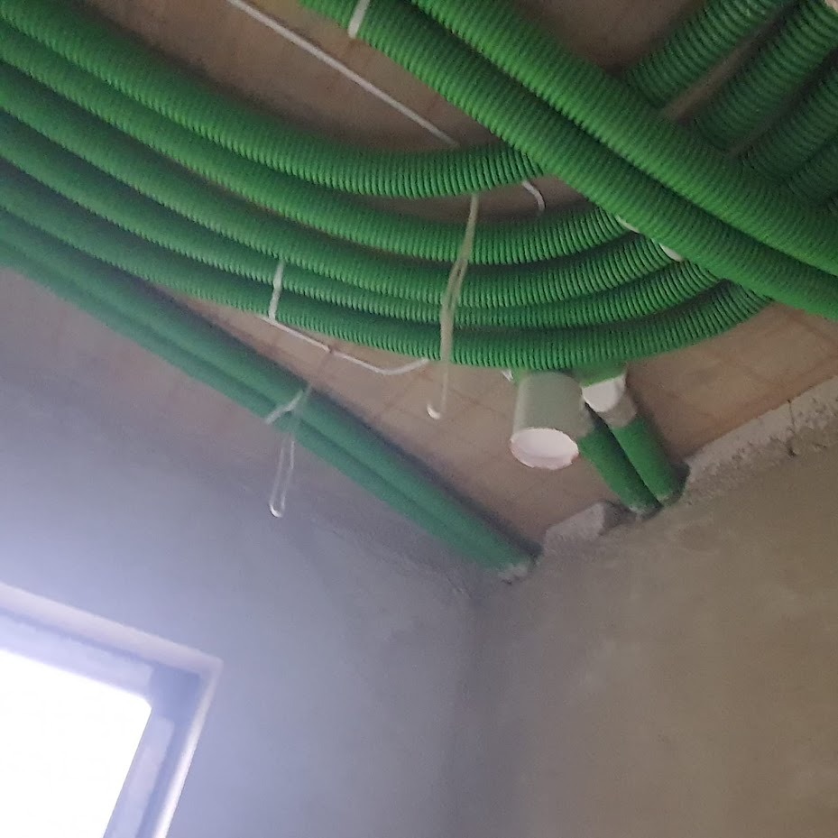 Zielone, karbowane rury instalacyjne przymocowane do sufitu, częściowo podwieszonego, z widocznym oknem w tle i elementami mocującymi.