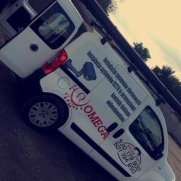 Omega - Biały samochód dostawczy z otwartymi drzwiami, oklejony reklamą firmy Omega, specjalizującej się w instalacji systemów alarmowych, CCTV i kontroli dostępu, z widocznymi numerami telefonów...