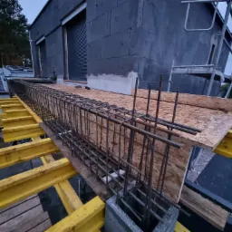 Wiązanie zbrojenia na stropie domu w trakcie budowy, widoczne szalunki i ściany budynku z izolacją.