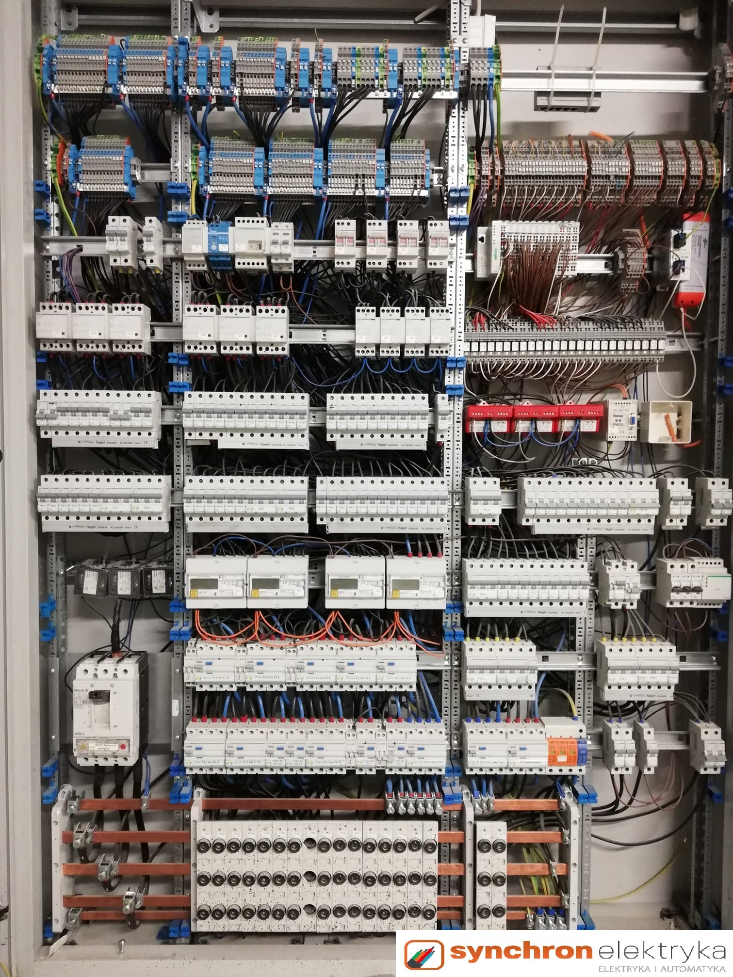 Rozdzielnica elektryczna z licznymi zabezpieczeniami, przewodami i listwami zaciskowymi, widoczne elementy automatyki przemysłowej, całość w szarej obudowie.