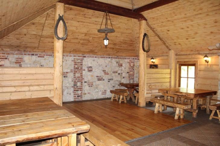 Rustykalna sala z drewnianymi ścianami, sufitami i podłogami, oświetlona wiszącą lampą z koła od wozu, z dekoracjami w postaci podków na słupach i stołami z ławami.