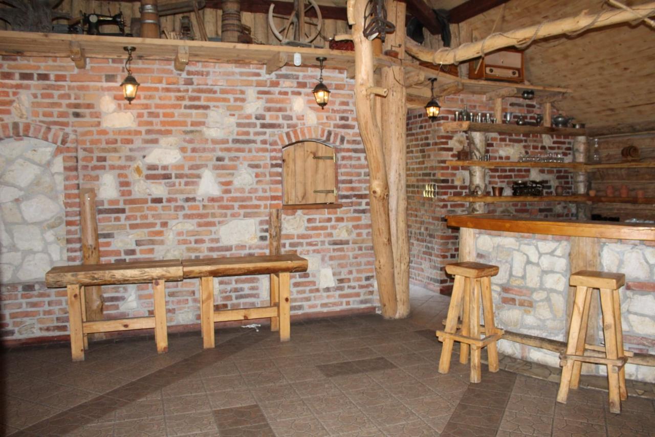 Rustykalne wnętrze baru z ceglanymi ścianami, drewnianymi belkami i stołkami barowymi, oświetlone wiszącymi lampami, z dekoracyjnymi półkami i elementami wystroju w stylu retro.