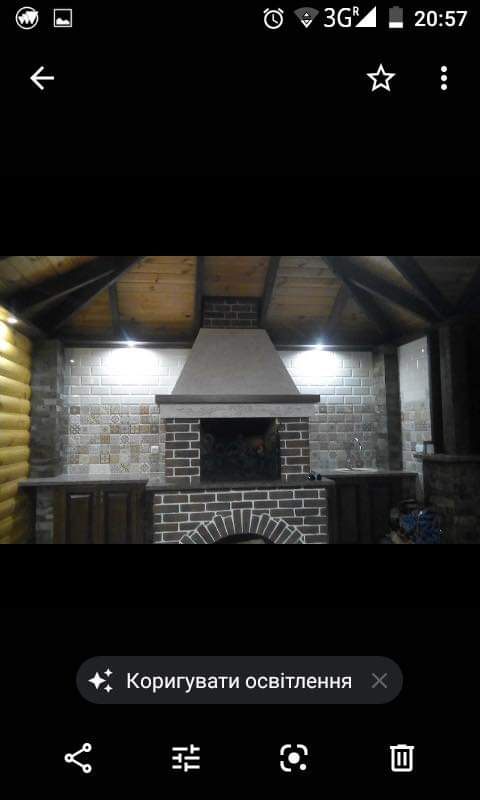 Zadaszony grill z cegły z łukowatym paleniskiem i okapem, wykończony płytkami i drewnem, oświetlony punktowo.