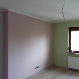 Cinek Marcin Barzowski - Wnętrze pokoju po remoncie: ściany pomalowane na różowo i jasnozielono, drewniana rama okienna, grzejnik pod oknem, drewniana podłoga, wystający kabel ze ściany.