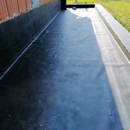 Cinek Marcin Barzowski - Hydroizolacja płaskiego dachu z papy bitumicznej, widoczne łączenia i fragment ściany budynku w trakcie budowy.