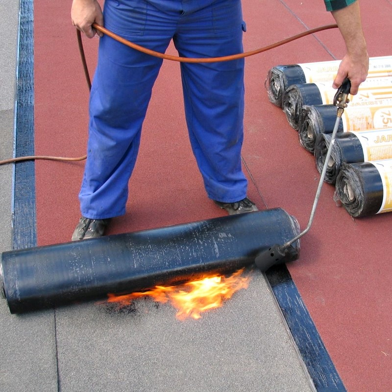 Dekarz przy użyciu palnika łączy papę termozgrzewalną na dachu, widoczne rolki papy marki JARO 7.5m.