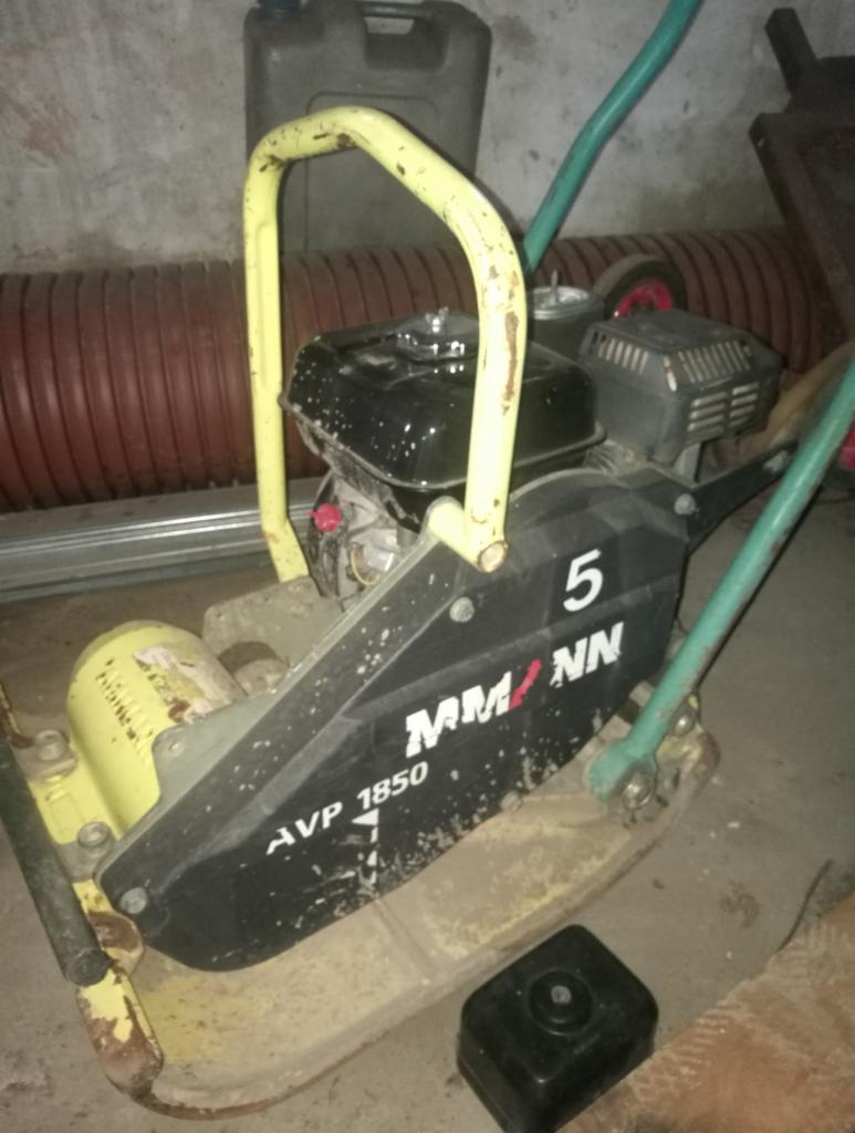 Używana zagęszczarka gruntu marki Ammann AVP 1850 z żółtą ramą i czarną obudową, widoczne ślady eksploatacji, tło stanowią rury i kanister.