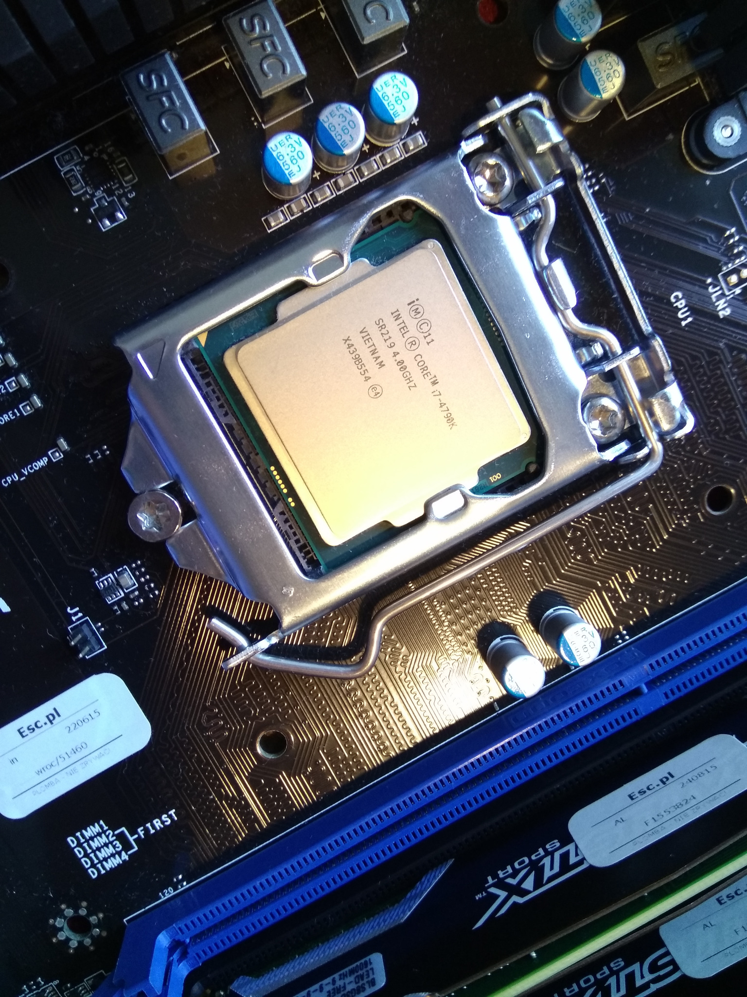 Zamknięte gniazdo procesora Intel Core i7-4790K na płycie głównej, widoczne elementy elektroniczne i sloty pamięci RAM, ujęcie z góry.