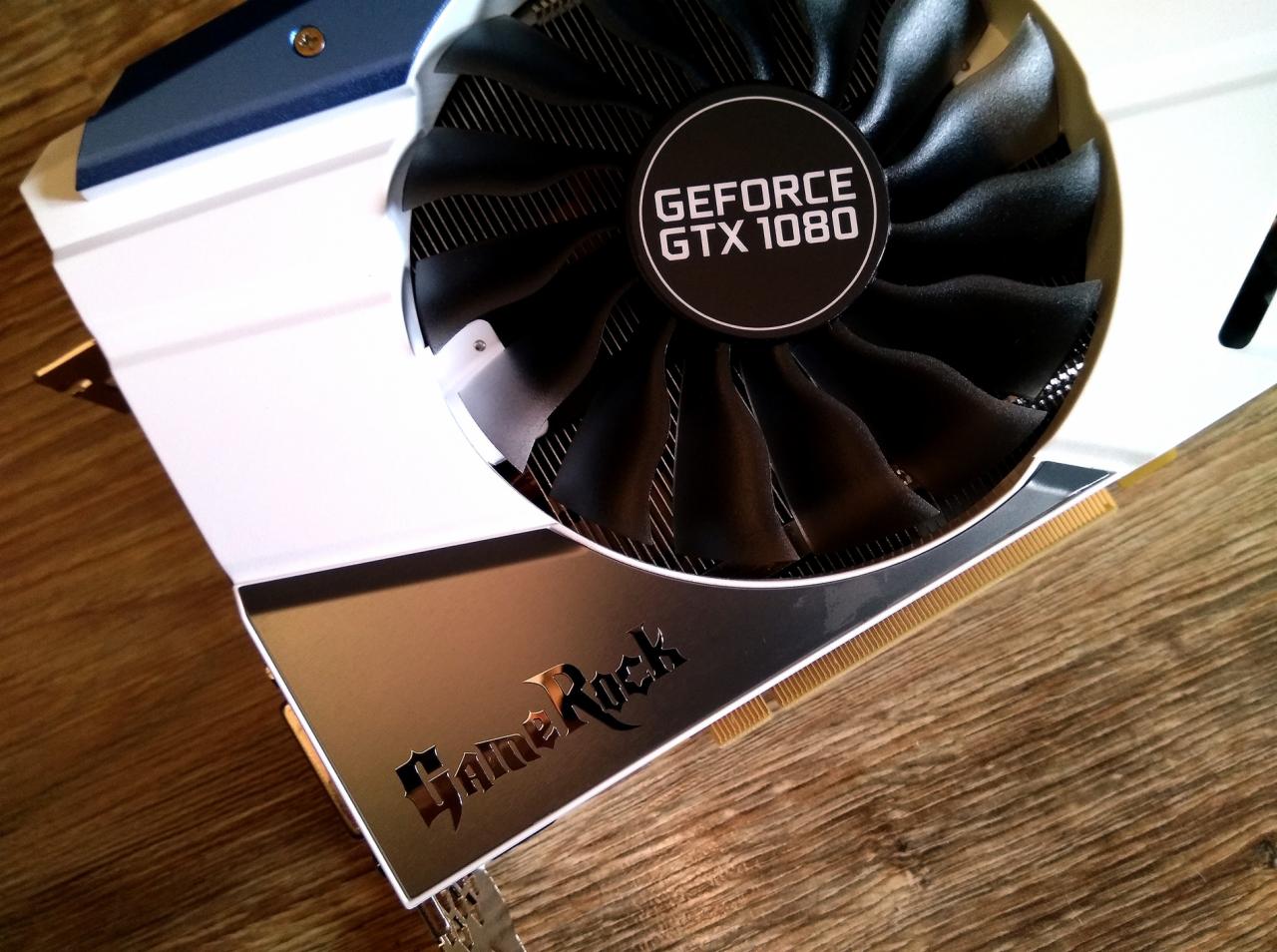 Karta graficzna GeForce GTX 1080 GameRock z białym radiatorem i czarnym wentylatorem, leżąca na drewnianej powierzchni.