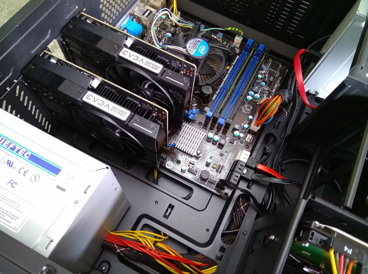 Wnętrze obudowy komputera stacjonarnego z zainstalowanymi dwiema kartami graficznymi EVGA GeForce GTX 1050 Ti, płytą główną z niebieskimi slotami RAM, zasilaczem Chieftec i widocznym okablowaniem...