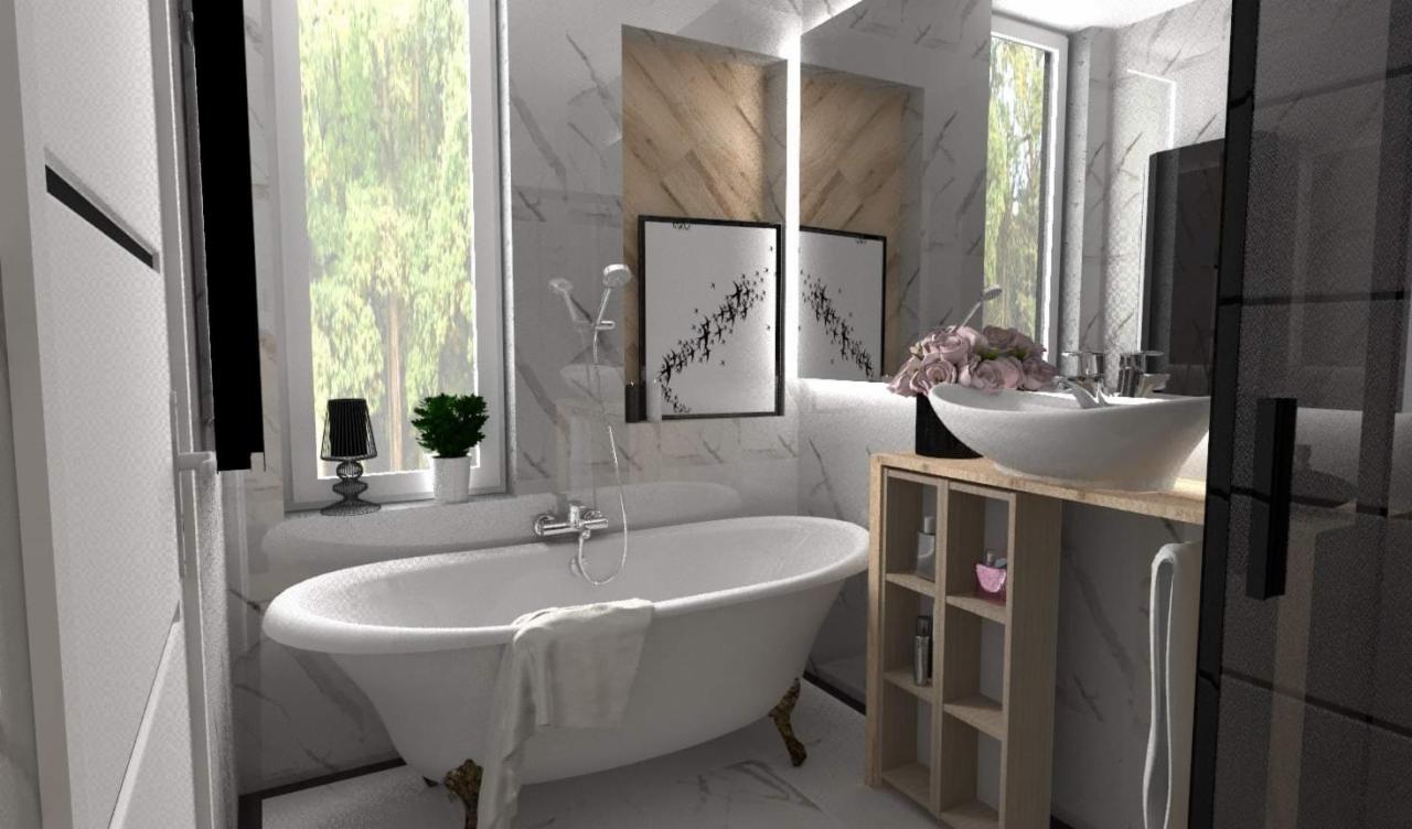 Elegancka łazienka z wolnostojącą wanną na złotych nóżkach, marmurowymi płytkami, umywalką nablatową i dekoracyjnymi obrazkami na ścianie.