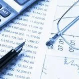 Kalkulator, długopis i okulary na wydruku z danymi finansowymi i wykresem, w chłodnej tonacji.