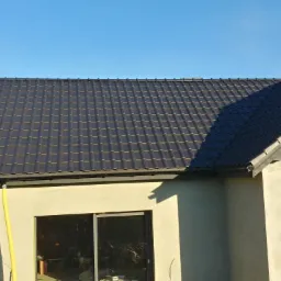 Nowoczesny dom jednorodzinny z grafitowym dachem z dachówki ceramicznej, widoczne obróbki blacharskie i rynna, elewacja w trakcie wykończenia.