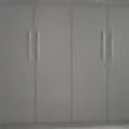 Szare, matowe drzwi szafy wnękowej z długimi, pionowymi uchwytami, widoczne na całej wysokości, z delikatnym cieniem na dolnej krawędzi.