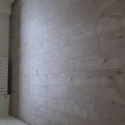 Ułożone panele podłogowe w odcieniach szarości z widocznym oknem i grzejnikiem w tle.