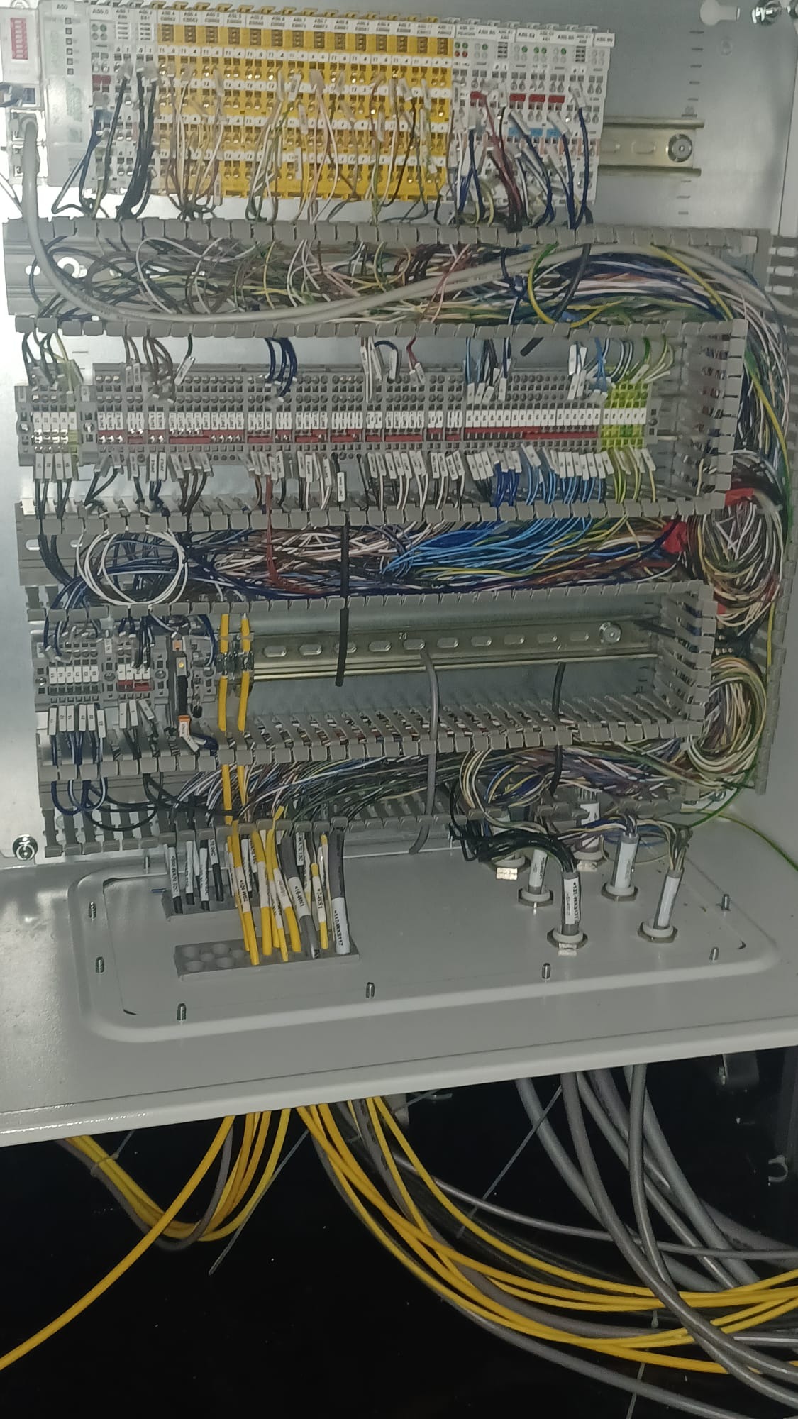 Rozdzielnica elektryczna z licznymi przewodami w różnych kolorach, uporządkowanymi w listwach. Widoczne złącza i oznaczenia na kablach.