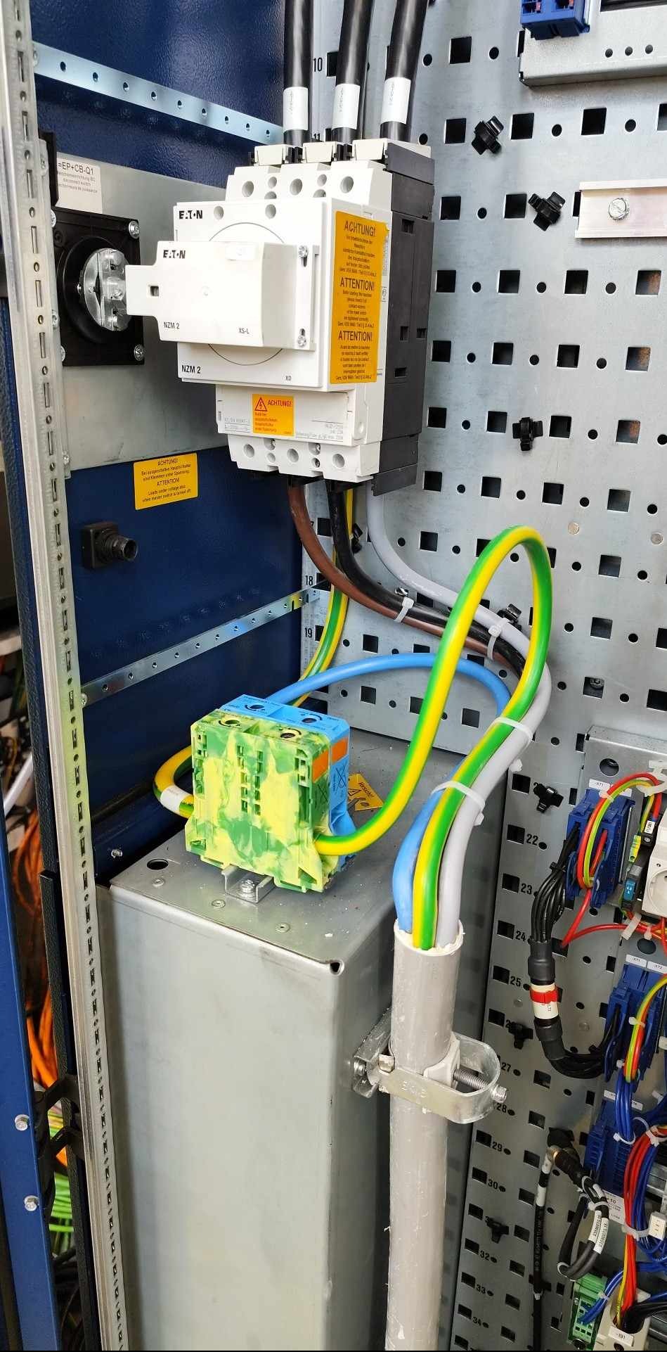 Szczegółowe ujęcie tablicy rozdzielczej z elementami marki EATON, widoczne przewody w kolorach: żółto-zielonym, niebieskim i brązowym. Elementy zamontowane na perforowanej płycie.