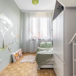 WD Developer Sp. z o.o - Pokój dziecięcy z motywem safari: malowidła zwierząt na ścianie, drewniana podłoga, białe meble i okno z delikatnymi zasłonami. Przytulna aranżacja.