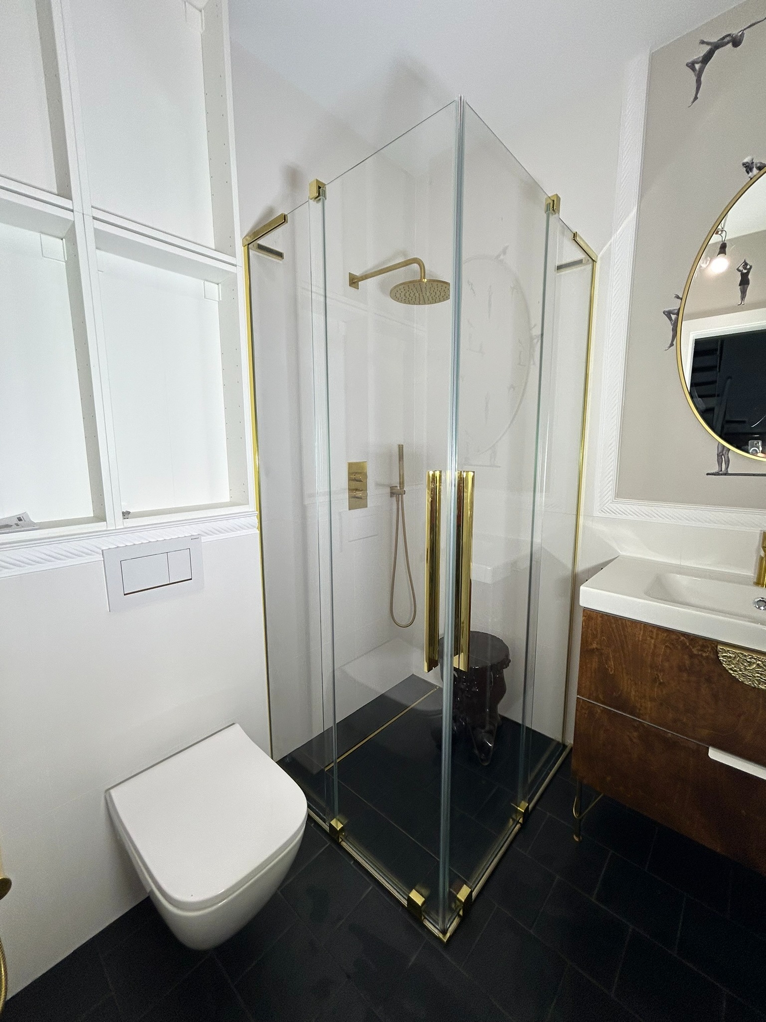 Nowoczesna łazienka z kabiną prysznicową typu walk-in z złotymi detalami, wiszącą toaletą, umywalką z szafką z forniru i czarną podłogą z płytek.