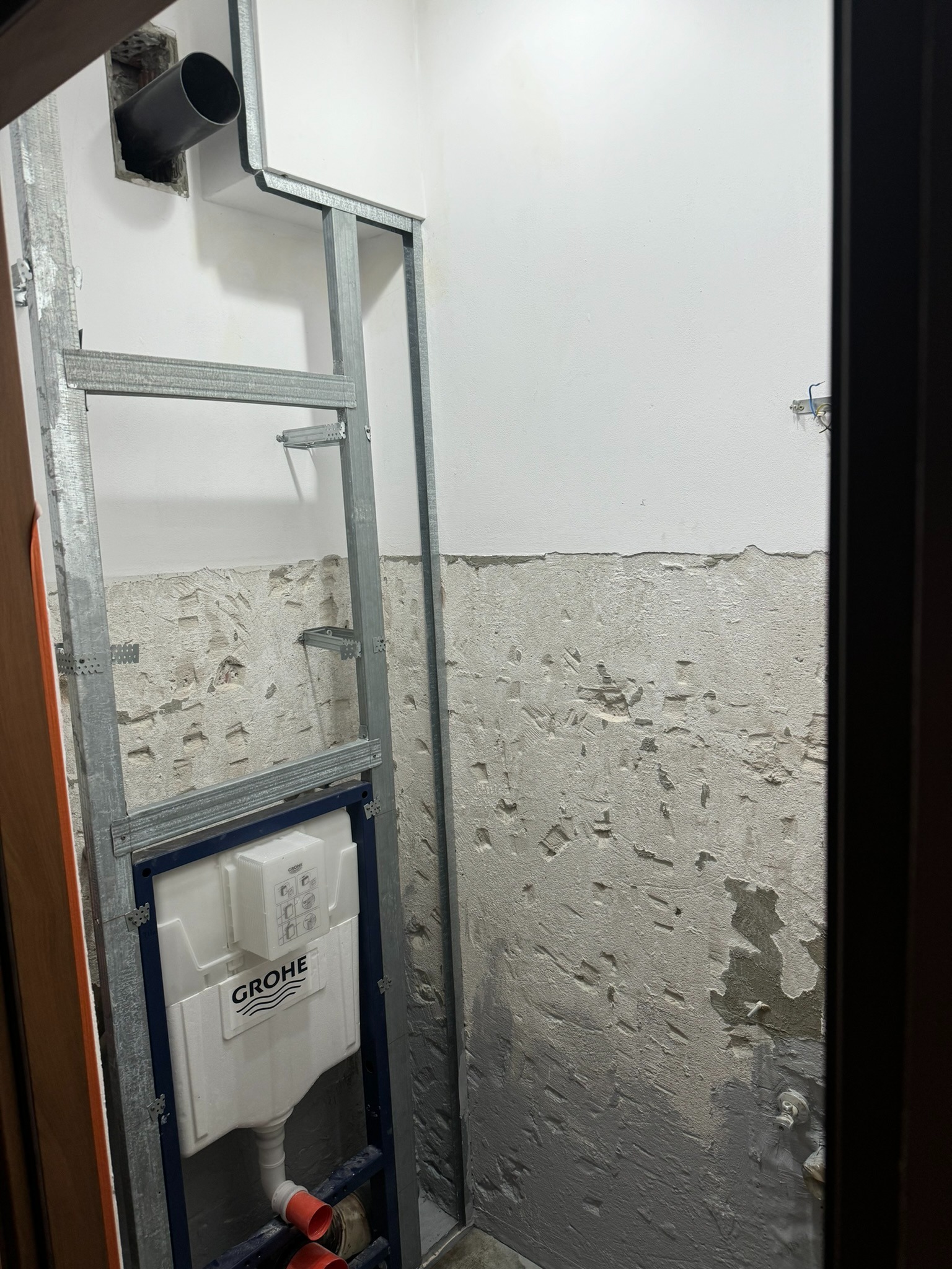 Stelaż podtynkowy Grohe zamontowany w łazience w trakcie prac, widoczne rury kanalizacyjne i fragment ściany z usuniętą glazurą.