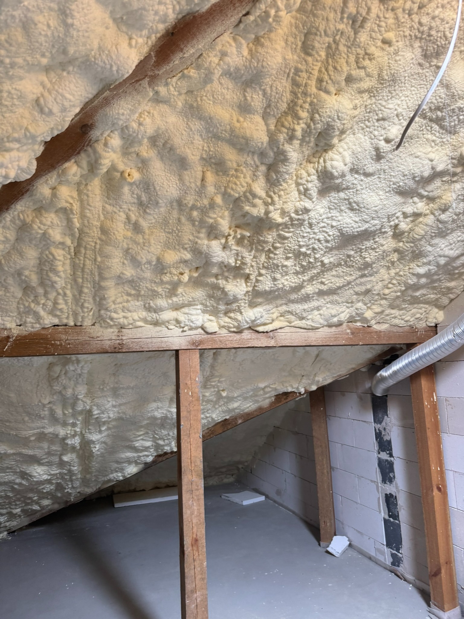 Poddasze ocieplone pianką PUR, widoczne drewniane elementy konstrukcyjne i fragment wentylacji. Aplikacja pianki na skośnych powierzchniach dachu.