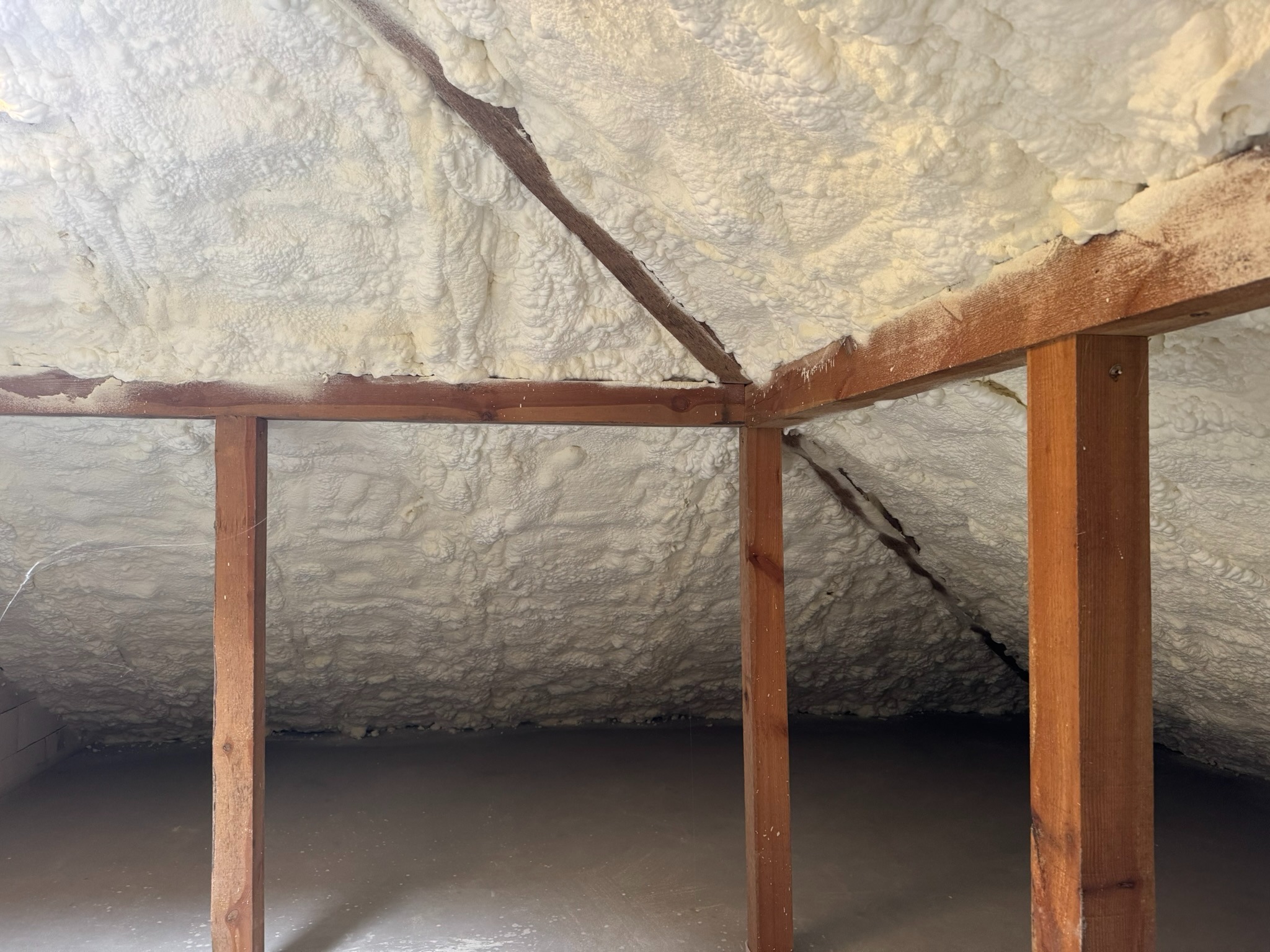 Poddasze ocieplone pianką PUR, widoczne drewniane elementy konstrukcyjne. Biała, nierówna powierzchnia pianki pokrywa skosy dachu i ściany.