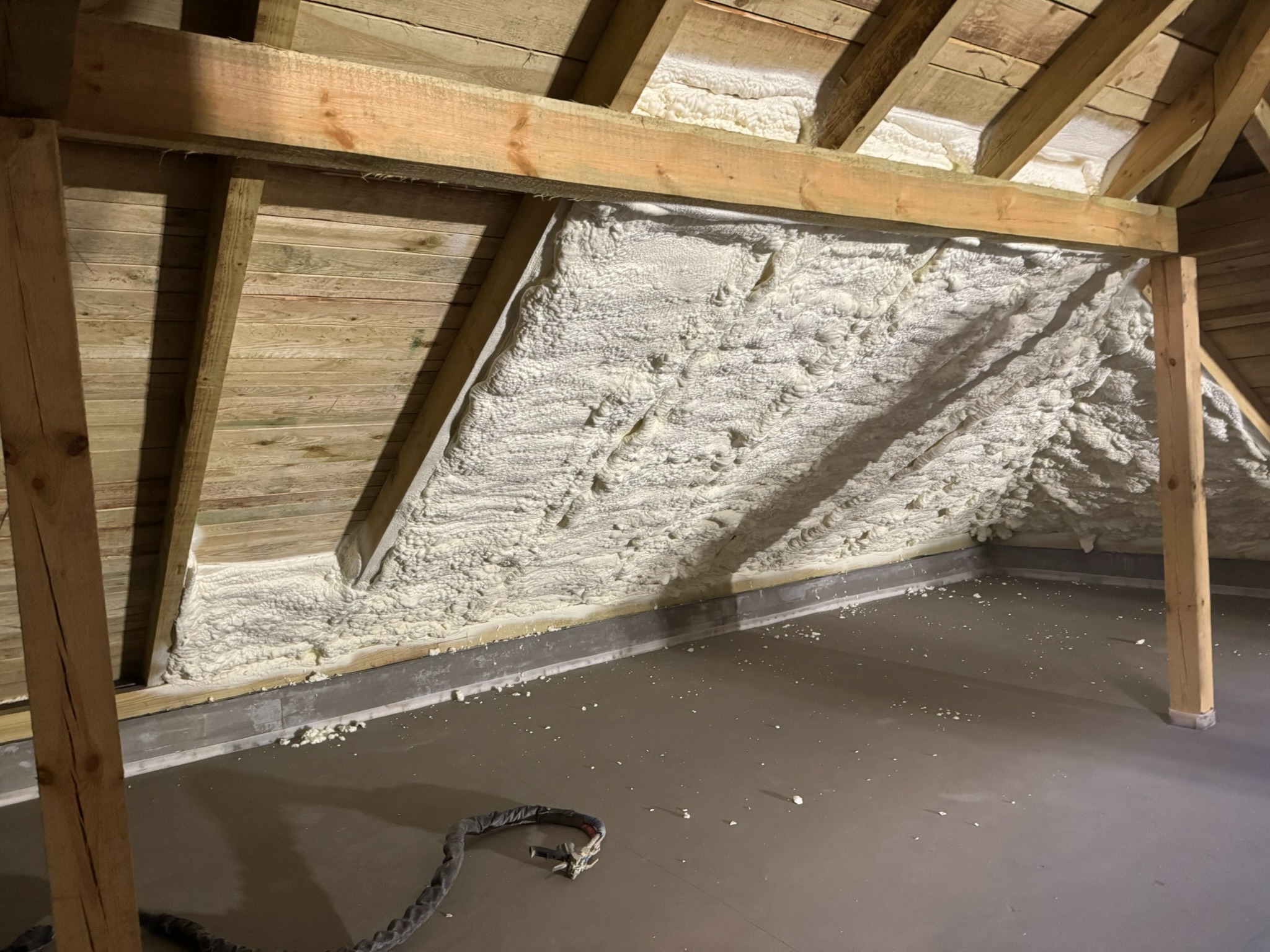 Poddasze z drewnianą konstrukcją i ociepleniem pianką PUR, widoczne krople pianki na podłodze, szary przewód leżący na posadzce.