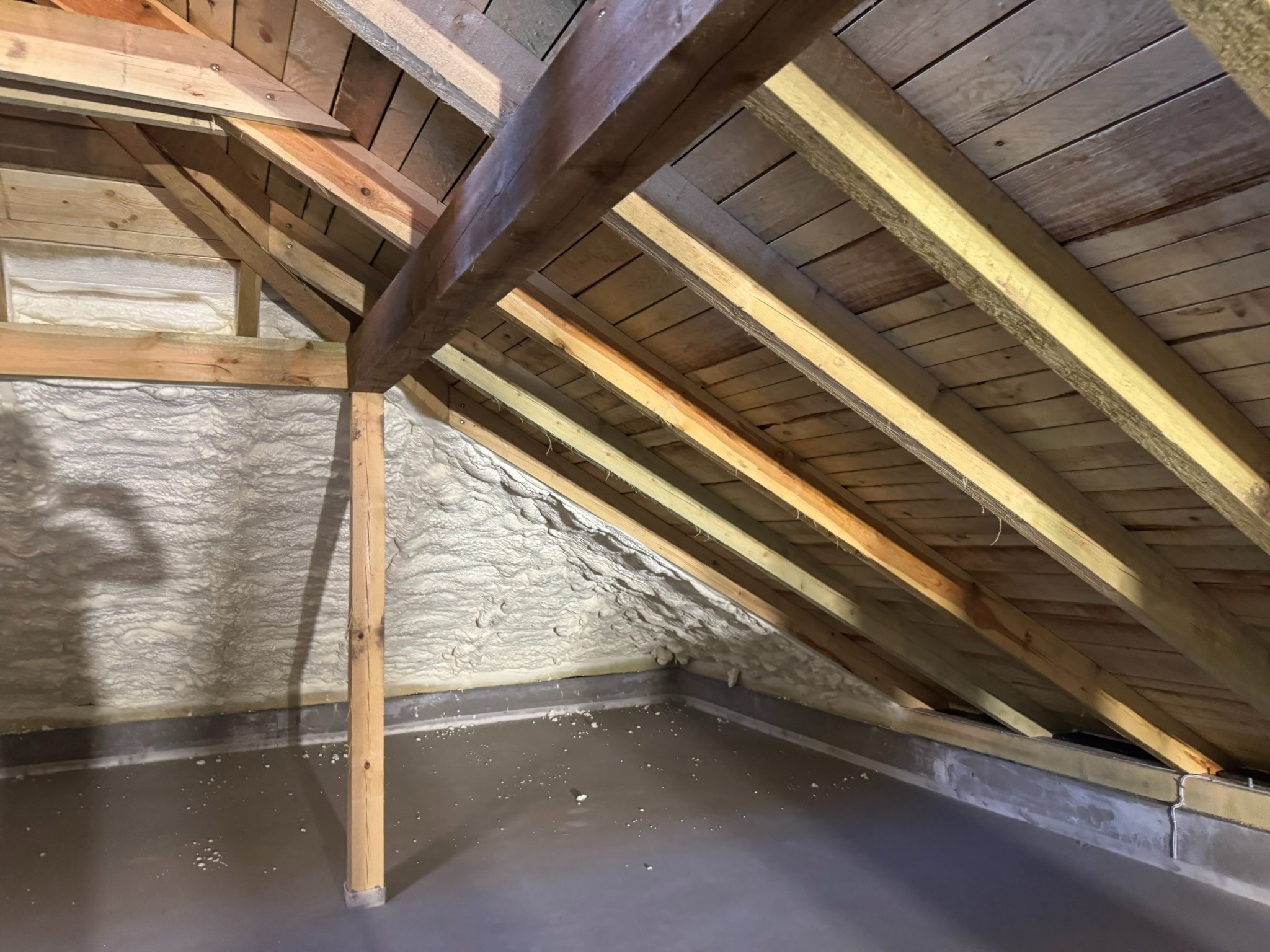 Poddasze z drewnianą konstrukcją i ociepleniem pianką PUR na ścianach, widoczne krokwie i słupki, szara podłoga. Detal: nierównomierna struktura pianki.