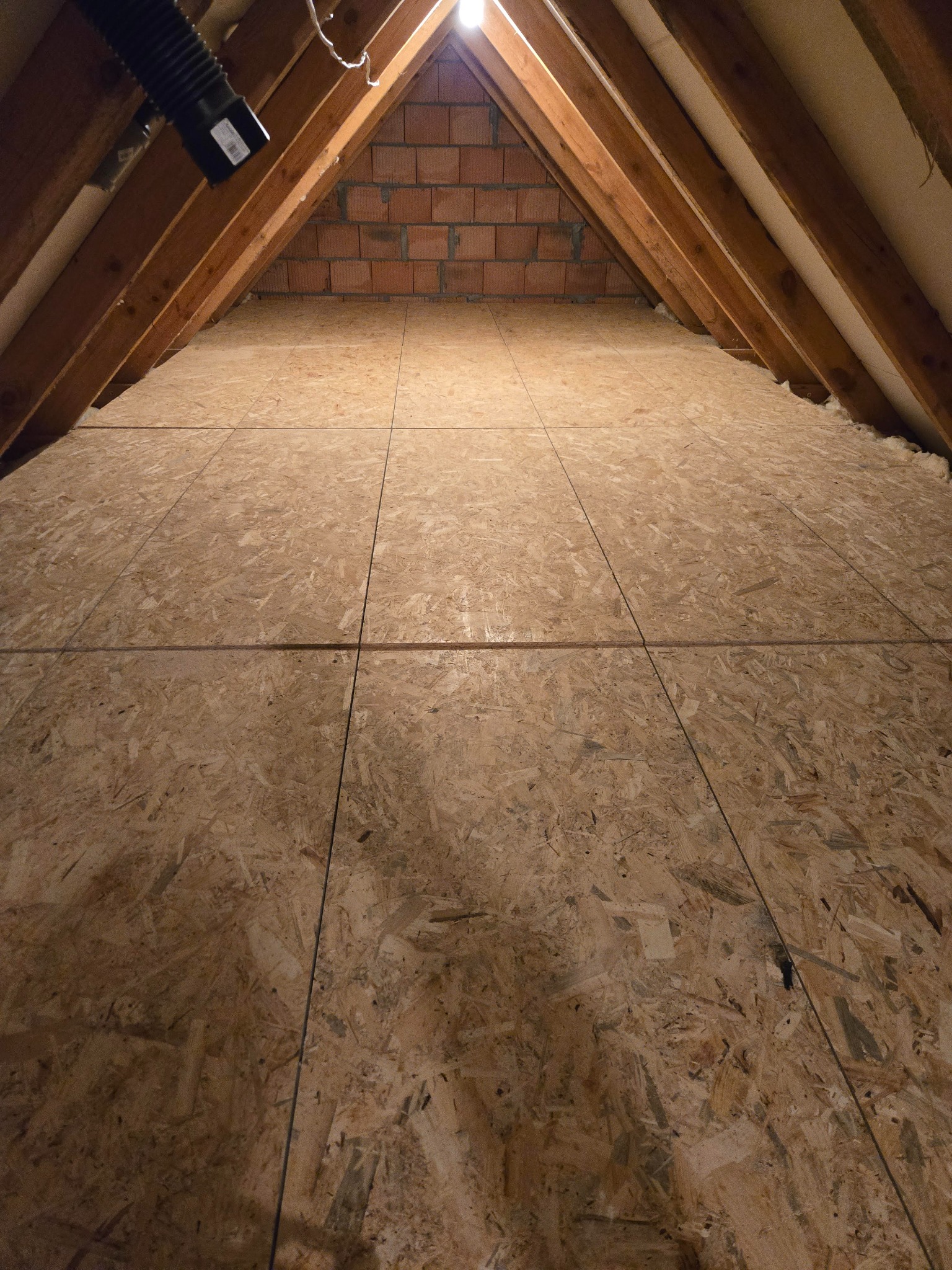 Płyty OSB na poddaszu z widoczną konstrukcją dachu i ociepleniem. Ujęcie z dołu, podkreślające geometrię i materiały wykończeniowe.