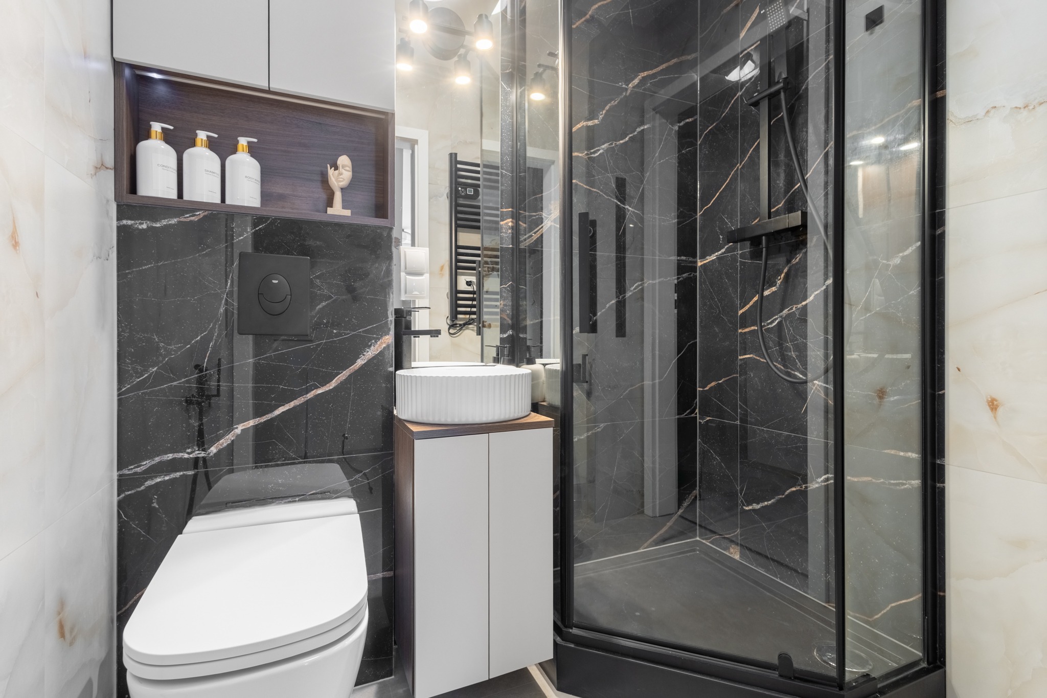 Nowoczesna łazienka z czarnymi marmurowymi płytkami, białą ceramiką i kabiną prysznicową z czarnymi ramami. Minimalistyczny design, oświetlenie LED.