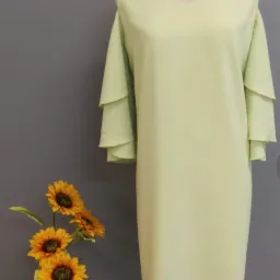 Jasnozielona sukienka z odkrytymi ramionami i dwuwarstwowymi rękawami na manekinie, dekorowana bukietem słoneczników na szarym tle.