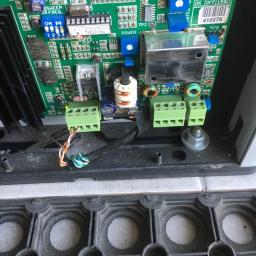 H.V.E - Otwarta obudowa urządzenia elektronicznego z widoczną zieloną płytką drukowaną, elementami elektronicznymi, złączami śrubowymi i przewodami. Widoczne ustawienia JP1 i JP2. Obok leży gumowa mata.