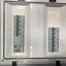 H.V.E - Otwarta biała skrzynka rozdzielcza z zainstalowanymi bezpiecznikami Hager, widoczne oznaczenia na bezpiecznikach i oznaczenie IP65 na obudowie.