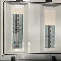 Otwarta biała skrzynka rozdzielcza z zainstalowanymi bezpiecznikami Hager, widoczne oznaczenia na bezpiecznikach i oznaczenie IP65 na obudowie.