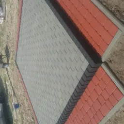 Fragment nowej nawierzchni z kostki brukowej w kolorach szaro-czerwonym, widoczny fragment samochodu osobowego, taczka i sadzonka drzewa na trawniku w tle.