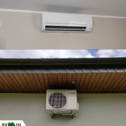 BIO - KLIM - Zewnętrzna i wewnętrzna jednostka klimatyzacji Mitsubishi Electric zamontowane na ścianie budynku, widoczny fragment dachu i logo firmy Bio-Klim w lewym dolnym rogu.