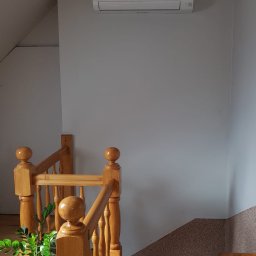 BIO - KLIM - Biały klimatyzator Mitsubishi zamontowany na ścianie nad drewnianą klatką schodową w domu w Ostrowie Wielkopolskim.