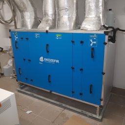 BIO - KLIM - Centrala wentylacyjna z rekuperacją, niebieska obudowa z czarnymi uchwytami, aluminiowe rury wentylacyjne, widoczne oznaczenia 'Nawiew', 'Wywiew', 'Czerpnia' i 'Wyrzutnia'.