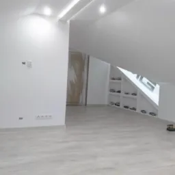 Jasne, przestronne poddasze po remoncie z białymi ścianami, drewnianą podłogą i wnękami z półkami, na których stoją małe samochody.