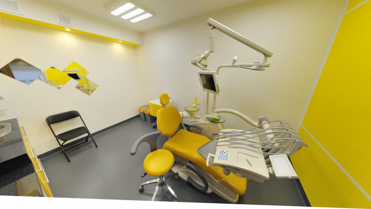Żółto-biały gabinet z fotelem dentystycznym, lampą operacyjną i narzędziami, uzupełniony o geometryczne lustra na ścianie.